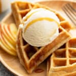 close up of apple waffles on brown plate with a scoop of vanilla ice cream and caramel drizzle