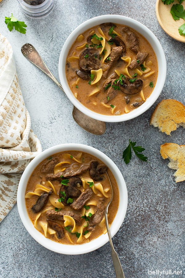 overhead of beef stroganoff soup in two white bowls with spoons