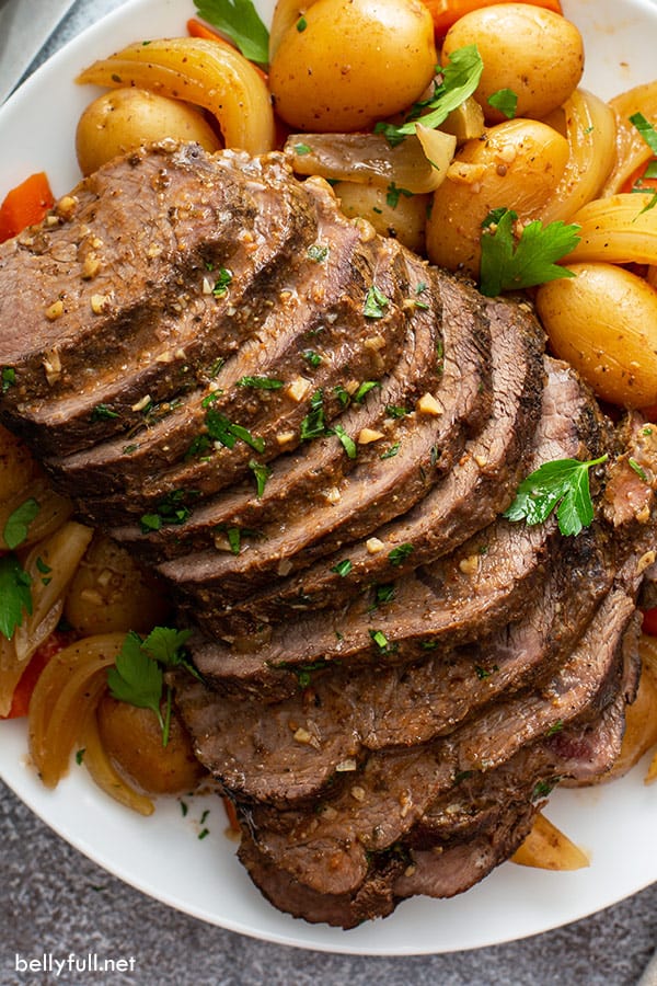 overhead sliced crock pot roast and vegetables with gravy on white plate
