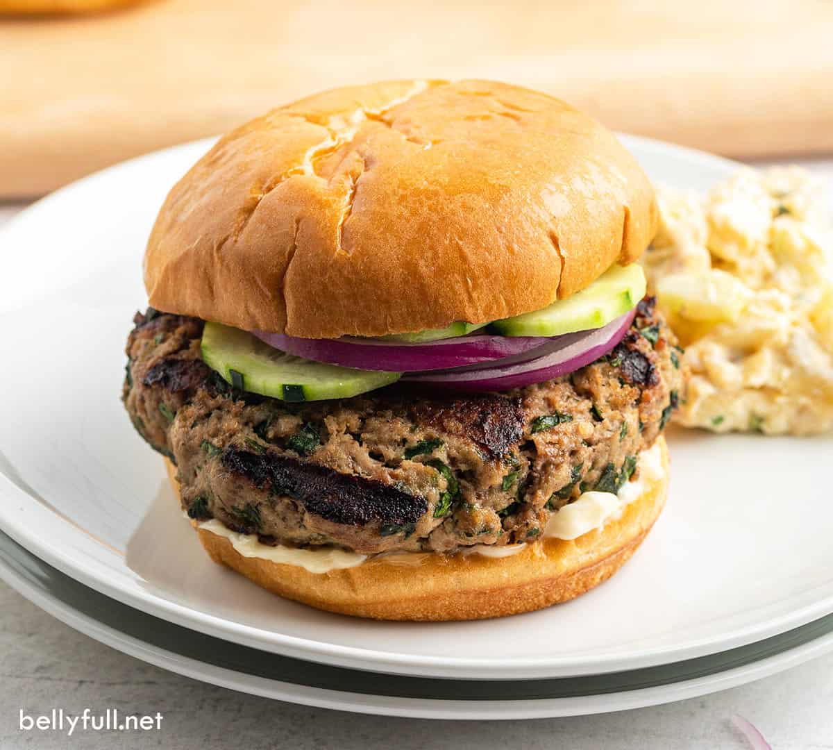 grilled turkey burger with cucumber and onion slices on white plate