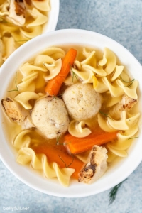 a bowl of matzo ball soup with carrots, noodles, and chicken