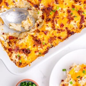 Cheesy potatoes casserole with a serving on a plate next to the baking dish