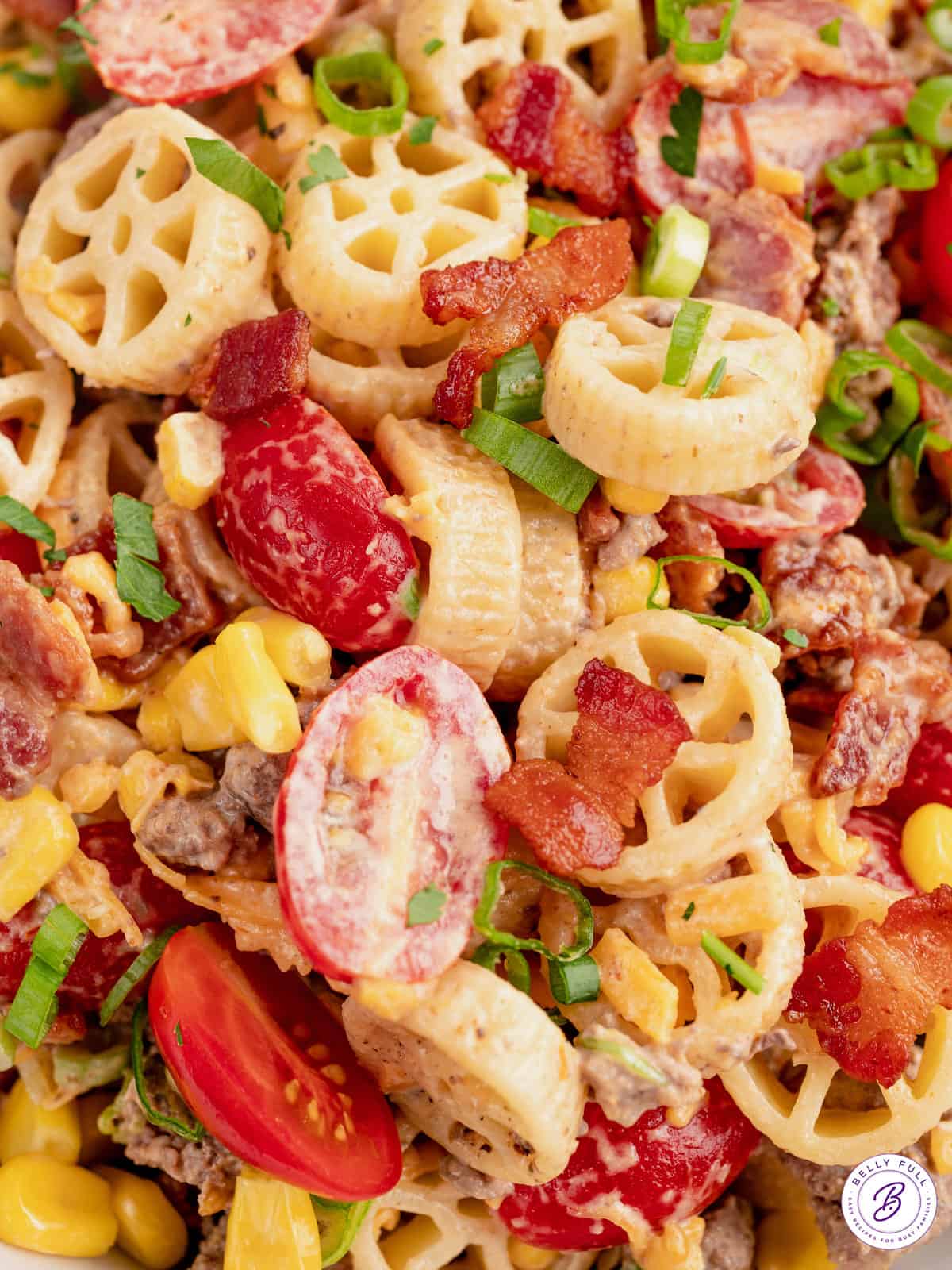 Close up creamy wagon wheel pasta salad with bacon and cherry tomatoes.