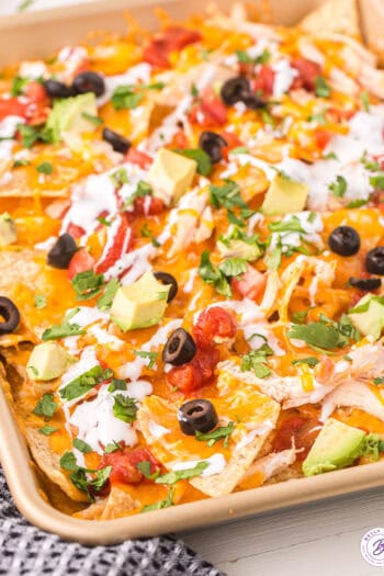 A baking sheet of chicken nachos topped with olives, avocado, and green onions