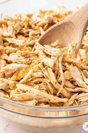 A wooden spoon stirring shredded chicken in a bowl